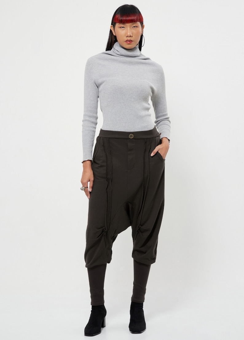May include: A woman is wearing a gray turtleneck sweater and brown, loose-fitting pants with a unique design. The pants have a wide leg and a gathered detail at the knees.
