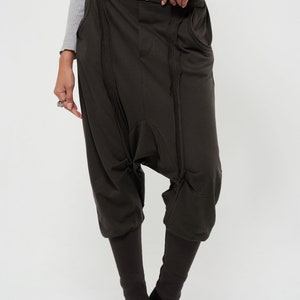 May include: Dark brown, loose-fitting pants with a unique design featuring multiple seams and pockets. The pants have a wide leg and a cropped length, ending just above the ankle.