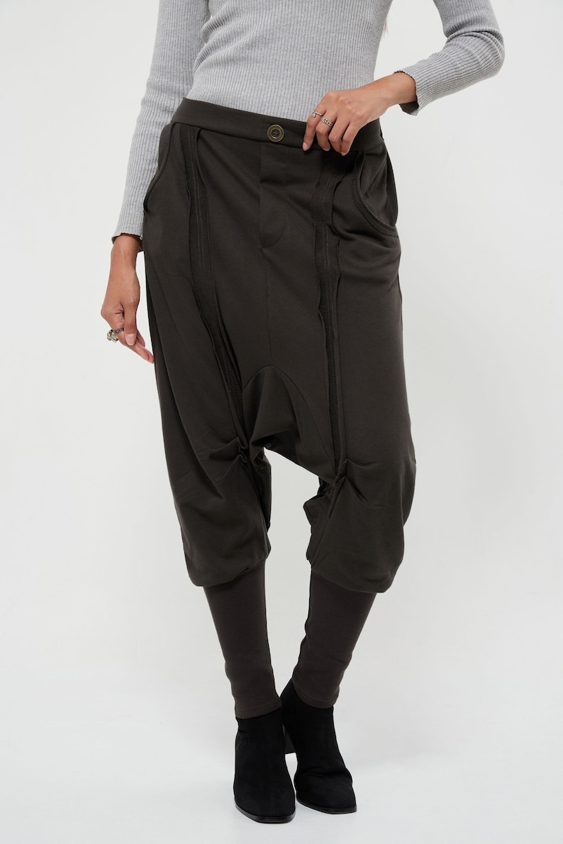 May include: Dark brown, loose-fitting pants with a unique design featuring multiple seams and pockets. The pants have a wide leg and a cropped length, ending just above the ankle.