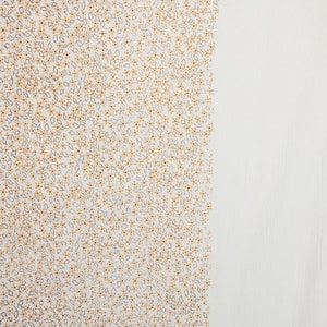 May include: White fabric with a small, repeating pattern of brown and yellow flowers.