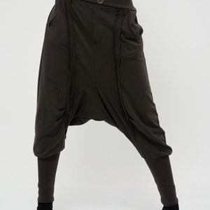 May include: Dark brown, loose-fitting pants with multiple zipper details and a wide leg. The pants have a low crotch and a relaxed fit.