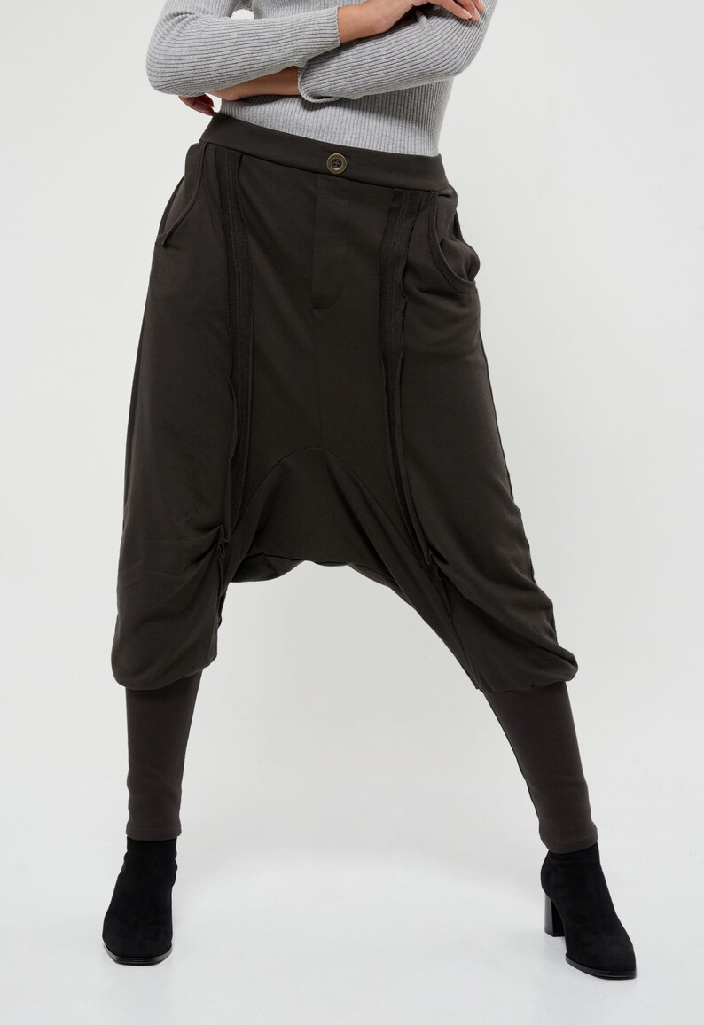 May include: Dark brown, loose-fitting pants with multiple zipper details and a wide leg. The pants have a low crotch and a relaxed fit.