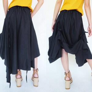 May include: A black asymmetrical skirt with a gathered design and tie details. The skirt is made of a soft, flowing fabric and has a relaxed fit.