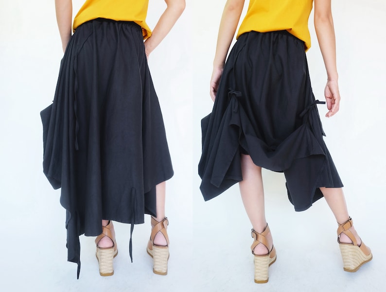 May include: A black asymmetrical skirt with a gathered design and tie details. The skirt is made of a soft, flowing fabric and has a relaxed fit.