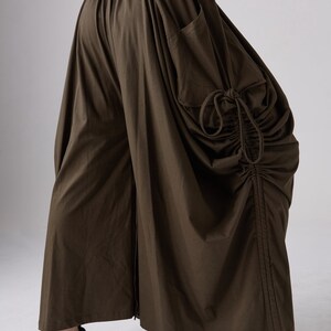 May include: A brown, loose-fitting, wide-leg pant with a drawstring detail on the side. The pant has a large pocket on the right side.