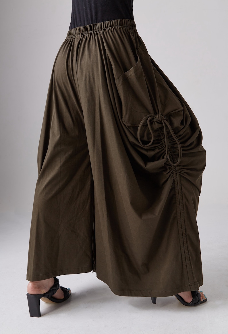 May include: A brown, loose-fitting, wide-leg pant with a drawstring detail on the side. The pant has a large pocket on the right side.