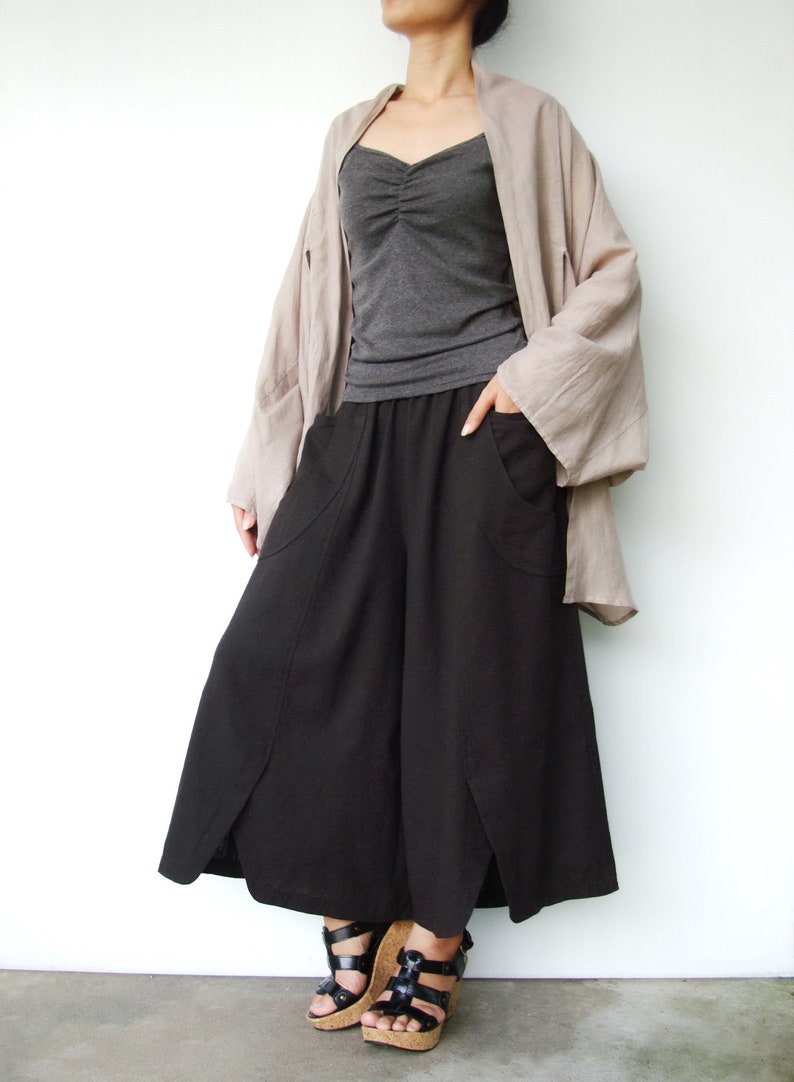 May include: A woman wearing a black wide-leg pants with a long, loose-fitting, light brown cardigan. She is wearing black sandals with cork wedges.