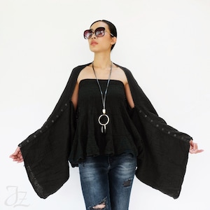 May include: A black kimono-style cardigan with long sleeves and button closures. The cardigan is worn over a black strapless top and blue jeans. The person is wearing sunglasses.