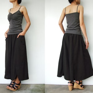 May include: A woman is wearing a gray tank top and a black maxi skirt with pockets. The skirt has a slight A-line shape and is flowy. She is wearing brown sandals.