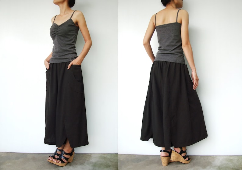 May include: A woman is wearing a gray tank top and a black maxi skirt with pockets. The skirt has a slight A-line shape and is flowy. She is wearing brown sandals.