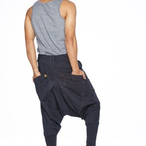 May include: A person wearing a gray tank top and dark blue pants with a unique design. The pants have a loose fit and a gathered look around the knees. The person is wearing black sneakers.