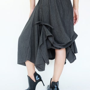 May include: A charcoal gray asymmetrical skirt with a gathered detail at the front. The skirt is made of a soft, drapey fabric and has a relaxed fit. The model is wearing the skirt with black heeled ankle boots.