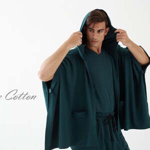 May include: A dark green hooded robe with a long, flowing design. The robe has a button on the left side and a pocket on the right side. The text "Joozie Cotton" is visible in the lower left corner of the image.