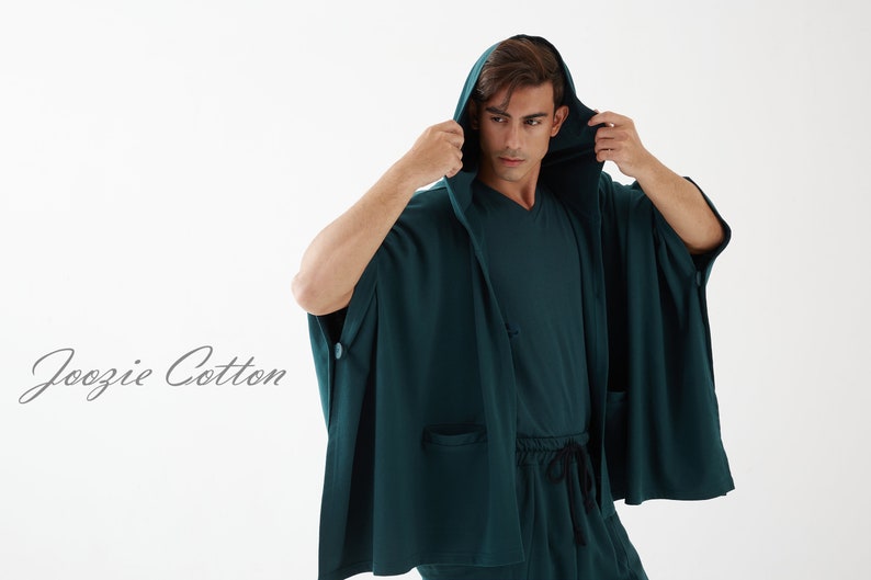 May include: A dark green hooded robe with a long, flowing design. The robe has a button on the left side and a pocket on the right side. The text "Joozie Cotton" is visible in the lower left corner of the image.