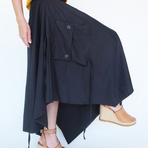May include: A black asymmetrical skirt with a large cargo pocket and a drawstring tie. The skirt is made of a lightweight fabric and has a flowing silhouette.