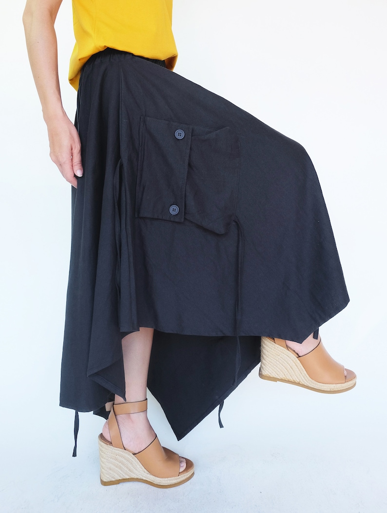 May include: A black asymmetrical skirt with a large cargo pocket and a drawstring tie. The skirt is made of a lightweight fabric and has a flowing silhouette.