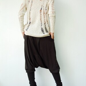 May include: A white, long-sleeved sweater with a distressed, open-weave design. The sweater is paired with black, loose-fitting pants.