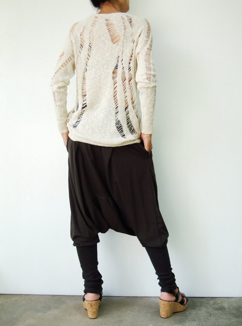 May include: A white, long-sleeved sweater with a distressed, open-weave design. The sweater is paired with black, loose-fitting pants.