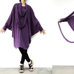 Puede incluir: Una t&uacute;nica larga, de color morado, con cuello de pico y mangas largas. Las mangas est&aacute;n fruncidas en las mu&ntilde;ecas y la t&uacute;nica es de corte holgado. La modelo lleva pantalones negros y sandalias.