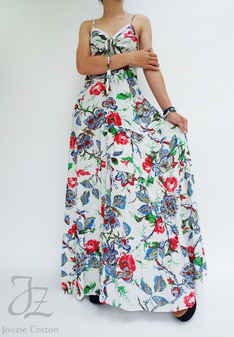 May include: A white maxi dress with a floral pattern featuring red and blue flowers and green leaves. The dress has spaghetti straps and a tie detail at the bust. The brand name "Joozie Cotton" is visible at the bottom.