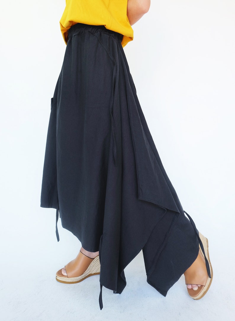 May include: A black asymmetrical skirt with a drawstring waist and side pockets. The skirt is made of a lightweight fabric and has a flowing silhouette.