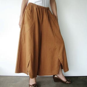 May include: A long, brown skirt with two large pockets and a slit on each side. The skirt is made of a soft, textured fabric and has a relaxed fit.