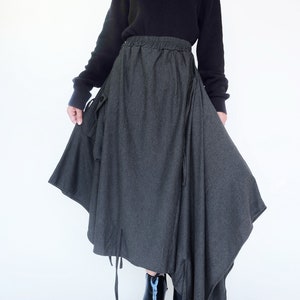 May include: A gray asymmetrical skirt with a drawstring waist and long ties hanging from the hem. The skirt is made of a soft, textured fabric and has a relaxed fit.
