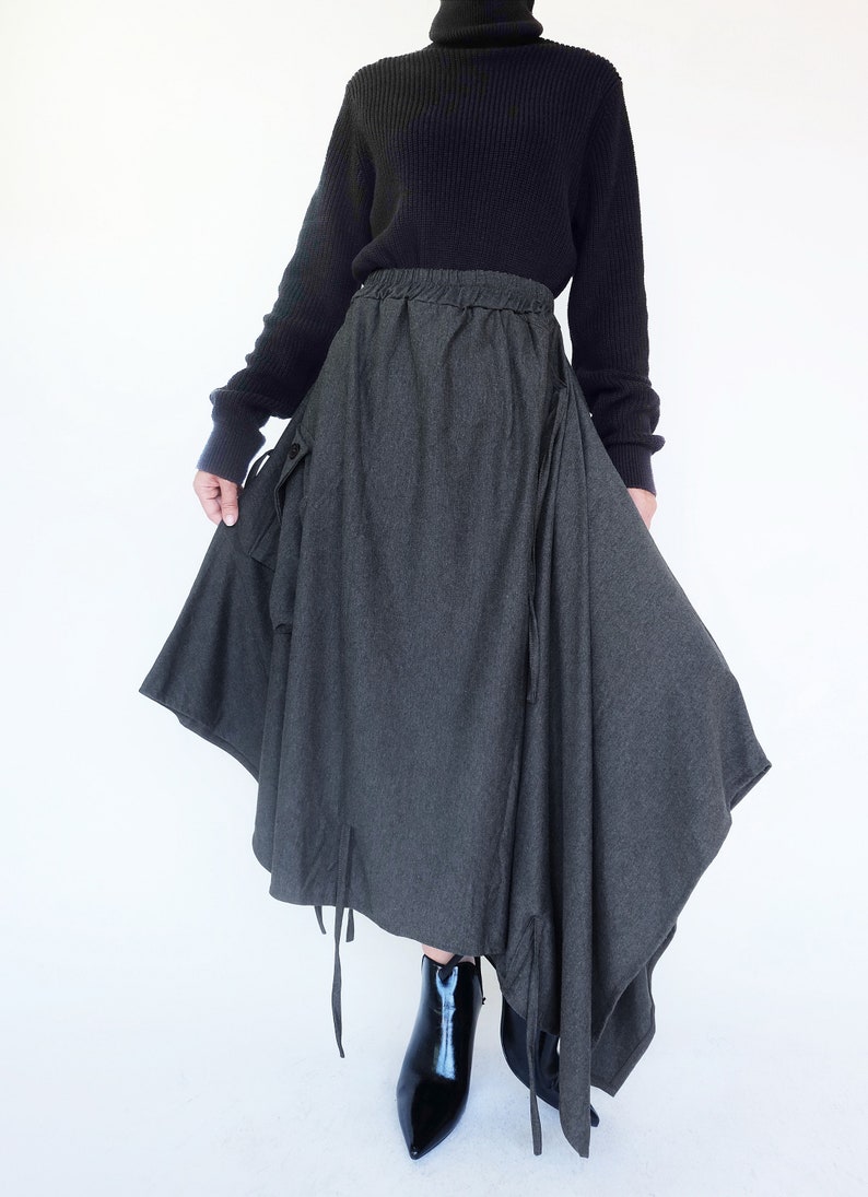 May include: A gray asymmetrical skirt with a drawstring waist and long ties hanging from the hem. The skirt is made of a soft, textured fabric and has a relaxed fit.