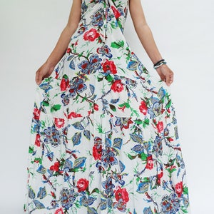 May include: A white maxi dress with a floral pattern featuring red and blue flowers and green leaves. The dress has spaghetti straps and a tiered skirt. The dress is a summer or beach style.