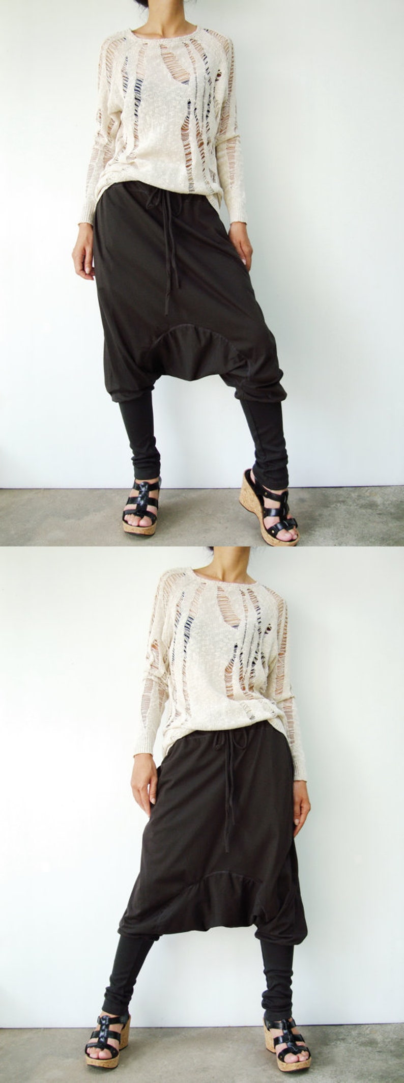 May include: A woman is wearing a white, open-knit sweater and brown, loose-fitting pants with a drawstring waist. She is wearing black sandals with cork soles.