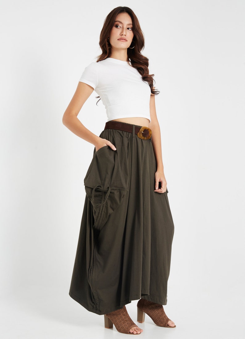 Puede incluir: Una mujer con un top blanco corto y una falda maxi verde oscuro con una hebilla de cintur&oacute;n marr&oacute;n grande. Lleva zapatos de tac&oacute;n abiertos marrones.