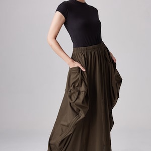 May include: A dark green maxi skirt with a gathered design and a button closure. The skirt has a relaxed fit and features pockets on the sides.