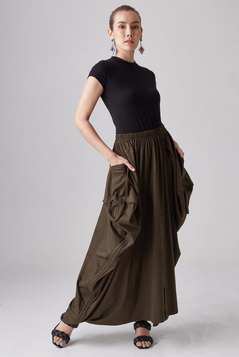May include: A dark green maxi skirt with a gathered design and a button closure. The skirt has a relaxed fit and features pockets on the sides.