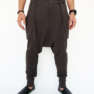 K&ouml;nnte beinhalten: Braune, lockere Hose mit einem einzigartigen Design, das eine gro&szlig;e Tasche auf jeder Seite aufweist. Die Hose hat einen breiten Bund und eine lockere Passform.