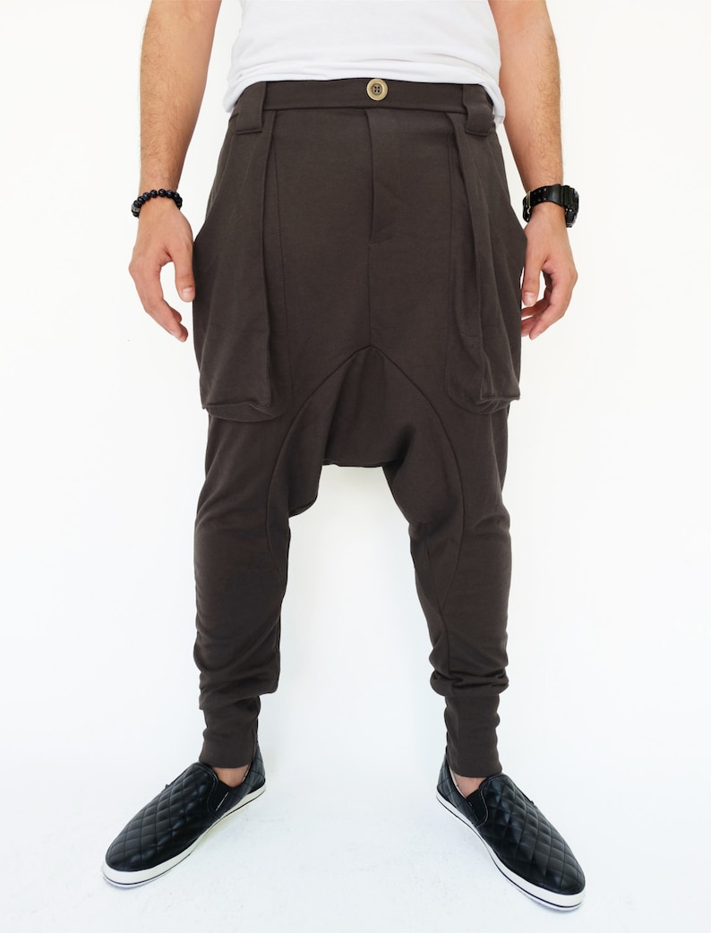 K&ouml;nnte beinhalten: Braune, lockere Hose mit einem einzigartigen Design, das eine gro&szlig;e Tasche auf jeder Seite aufweist. Die Hose hat einen breiten Bund und eine lockere Passform.