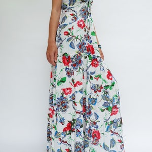 May include: A white maxi dress with a floral pattern featuring red, blue, and green accents. The dress has spaghetti straps and a tiered skirt. The floral design includes roses and other stylized flowers.