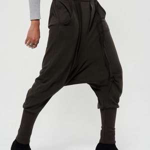 May include: Brown harem pants with a unique design featuring a gathered detail on the front and a button closure. The pants have a wide leg and a cropped length.