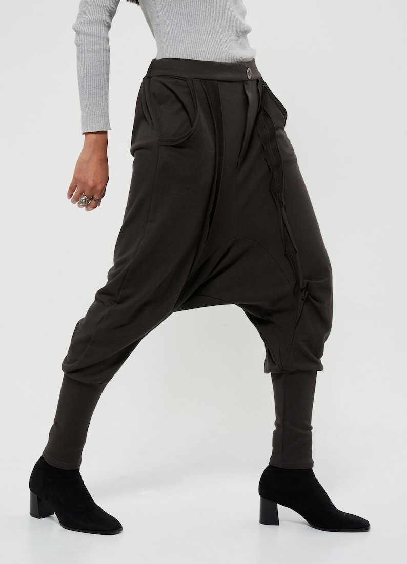 May include: Brown harem pants with a unique design featuring a gathered detail on the front and a button closure. The pants have a wide leg and a cropped length.