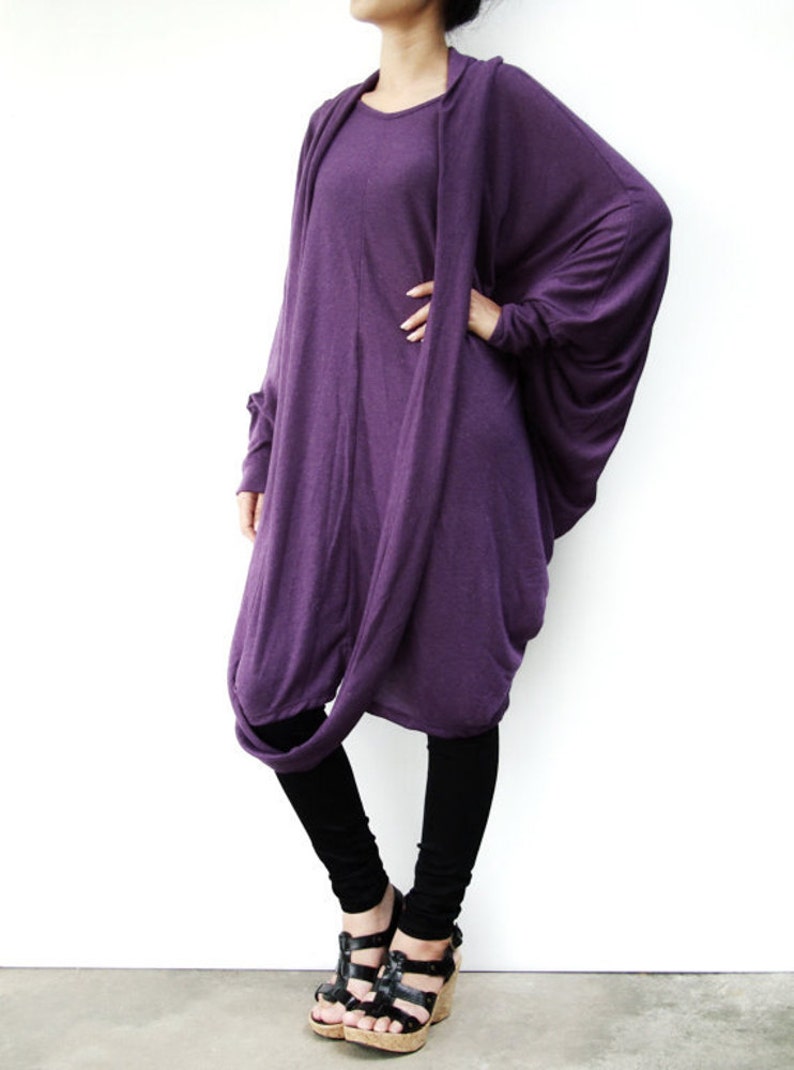 Puede incluir: Una t&uacute;nica larga y drapeada de color morado con mangas largas y cuello alto. La t&uacute;nica est&aacute; hecha de una tela suave y el&aacute;stica y se lleva con leggings negros y sandalias negras.