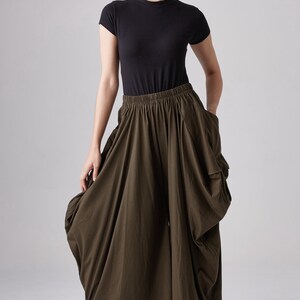 May include: A woman wearing a black mock neck shirt and olive green wide-leg pants with a gathered design. The pants have a wide, elastic waistband.