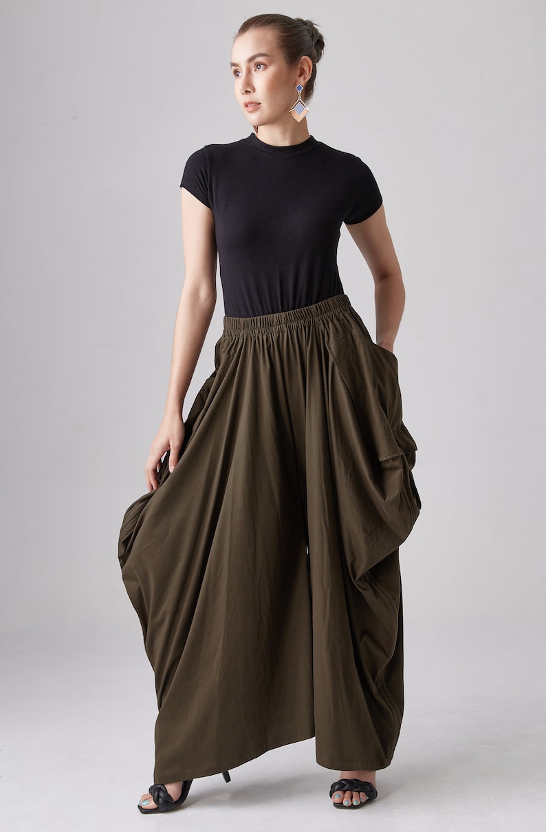 May include: A woman wearing a black mock neck shirt and olive green wide-leg pants with a gathered design. The pants have a wide, elastic waistband.