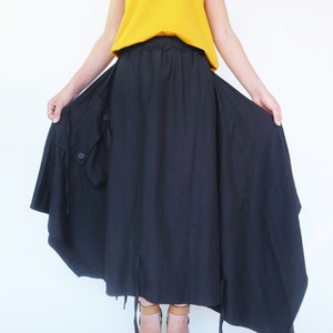 May include: A black asymmetrical skirt with a drawstring waist and a large pocket on the side. The skirt is worn with a mustard yellow tank top and brown heeled sandals.