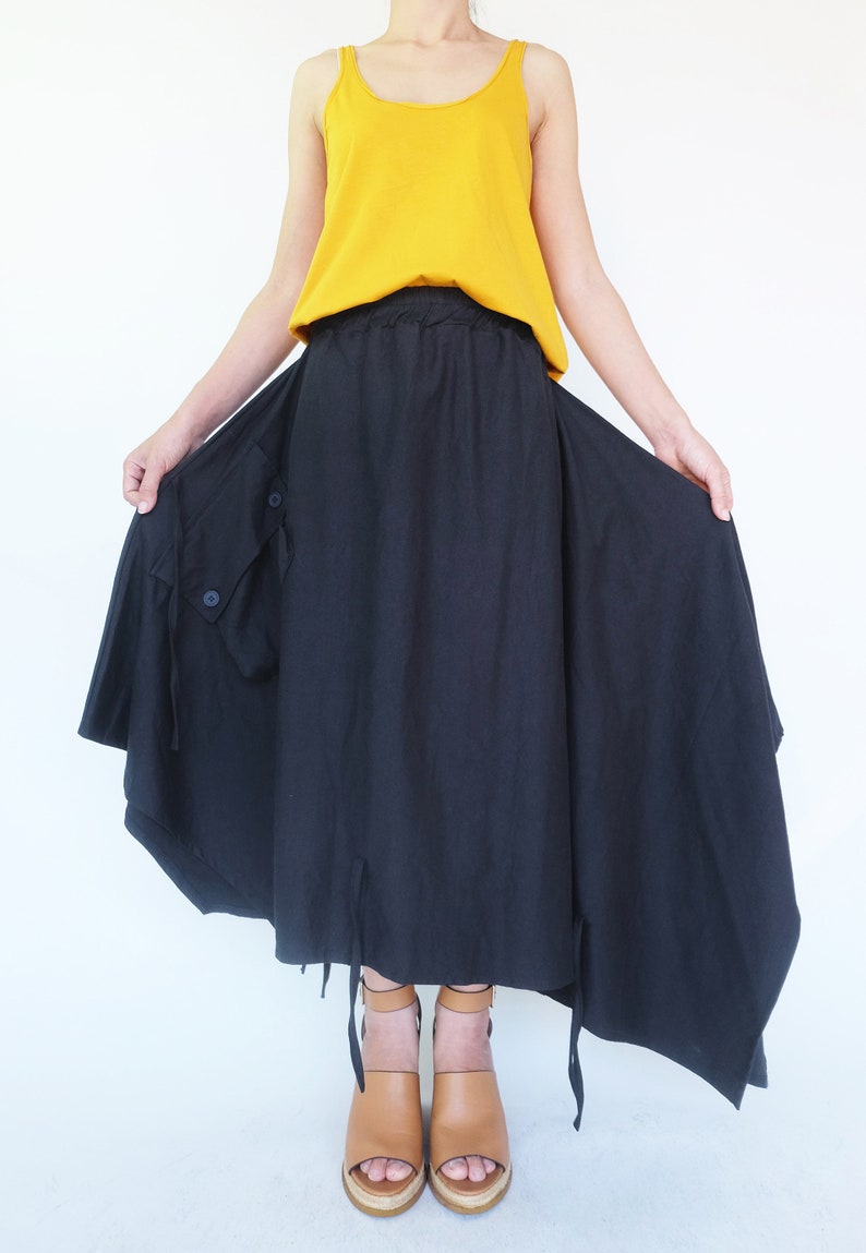 May include: A black asymmetrical skirt with a drawstring waist and a large pocket on the side. The skirt is worn with a mustard yellow tank top and brown heeled sandals.