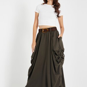Puede incluir: Una mujer lleva una camiseta blanca corta con un cintur&oacute;n marr&oacute;n y una falda larga de color verde oscuro con un dise&ntilde;o fruncido. Lleva zapatos de tac&oacute;n abiertos marrones.