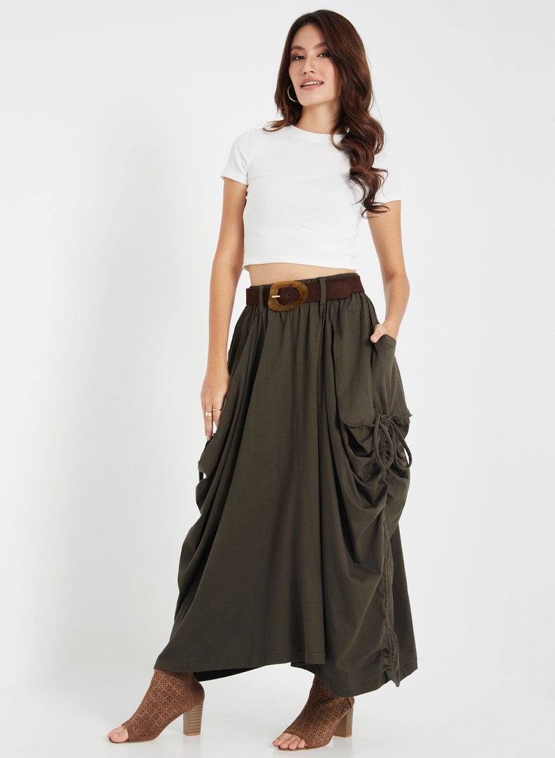 Puede incluir: Una mujer lleva una camiseta blanca corta con un cintur&oacute;n marr&oacute;n y una falda larga de color verde oscuro con un dise&ntilde;o fruncido. Lleva zapatos de tac&oacute;n abiertos marrones.