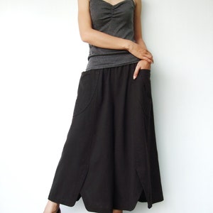May include: A woman wearing a gray tank top and a long black skirt with pockets. She is wearing black sandals with cork wedges.