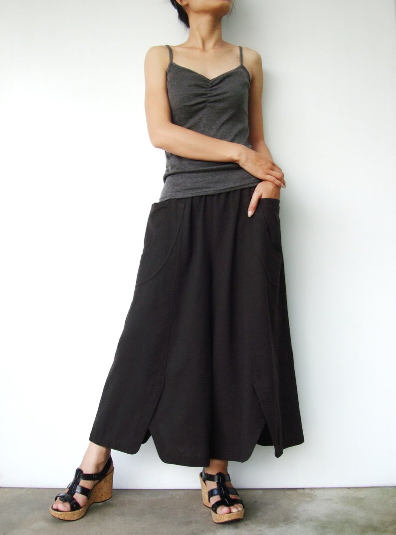 May include: A woman wearing a gray tank top and a long black skirt with pockets. She is wearing black sandals with cork wedges.