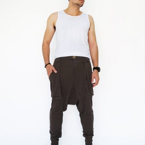 K&ouml;nnte beinhalten: Eine Person tr&auml;gt ein wei&szlig;es Tanktop und eine braune Hose mit einem einzigartigen Design. Die Hose hat eine lockere Passform und eine Raffung an der Schrittnaht. Die Person tr&auml;gt schwarze Schuhe.