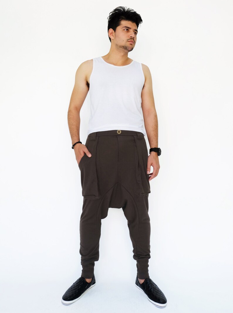 K&ouml;nnte beinhalten: Eine Person tr&auml;gt ein wei&szlig;es Tanktop und eine braune Hose mit einem einzigartigen Design. Die Hose hat eine lockere Passform und eine Raffung an der Schrittnaht. Die Person tr&auml;gt schwarze Schuhe.