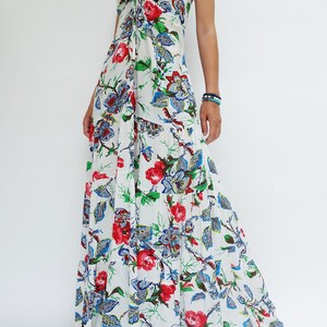 May include: White maxi dress with a floral print featuring red roses, blue and green leaves. The dress has spaghetti straps and a tie detail at the bust. The tiered skirt flows to the floor, creating a bohemian style.